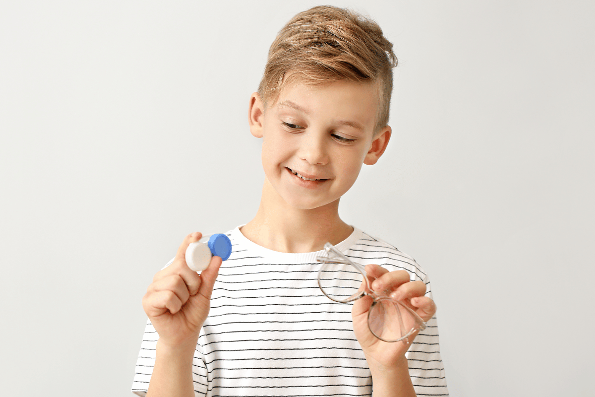 a young boy holding a contact lens case in one hand and a pair of glasses in the other hand