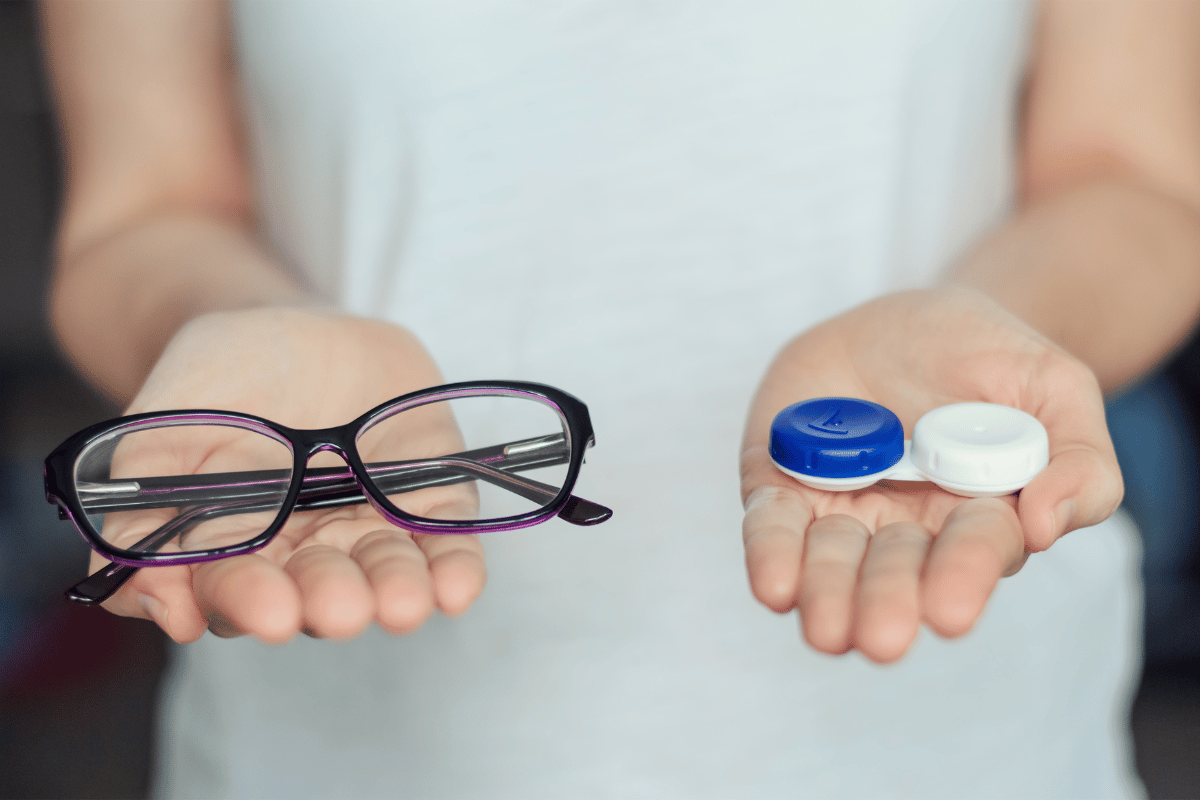 close-up of a woman's hands holding a contact lens case in one hand and a pair of glasses in the other