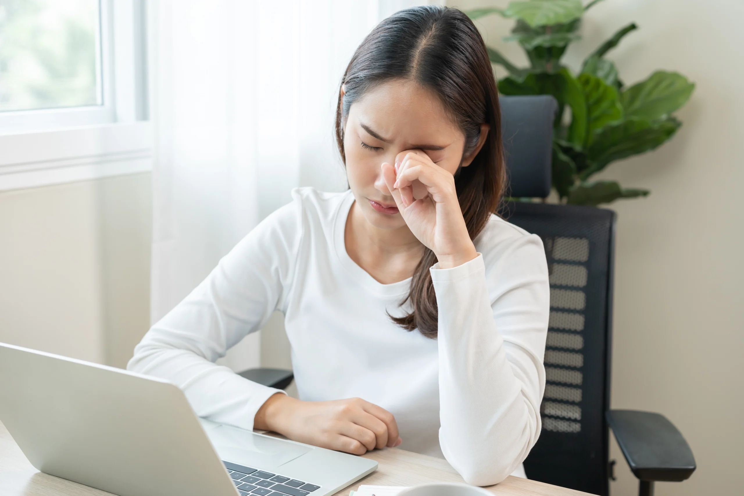 A young woman working on a computer rubs her dry tired eyes.