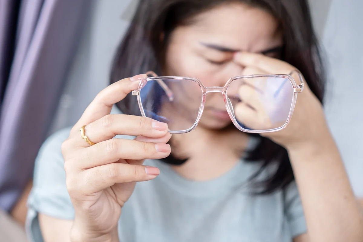 A woman holds her glasses in one hand and rubs the bridge of her nose with the other.